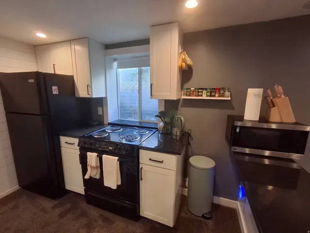 White shaker-style cabinetry, dark countertops, built-in range, and a window for natural light