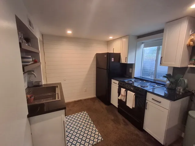 Compact kitchen featuring white cabinetry, black countertops, a black electric range, and a stainless steel sink