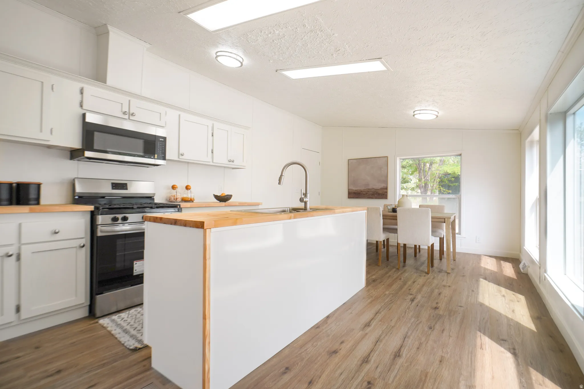 Modern kitchen featuring white cabinetry, butcher block countertops, stainless steel appliances, a kitchen island with an integrated sink, and wood-finish flooring