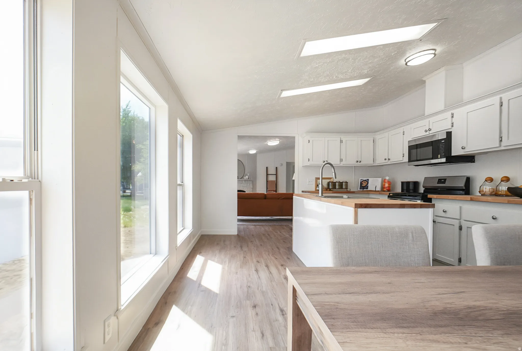 Full bank of windows, wood-finish flooring, white cabinetry, wood countertops, and stainless steel appliances