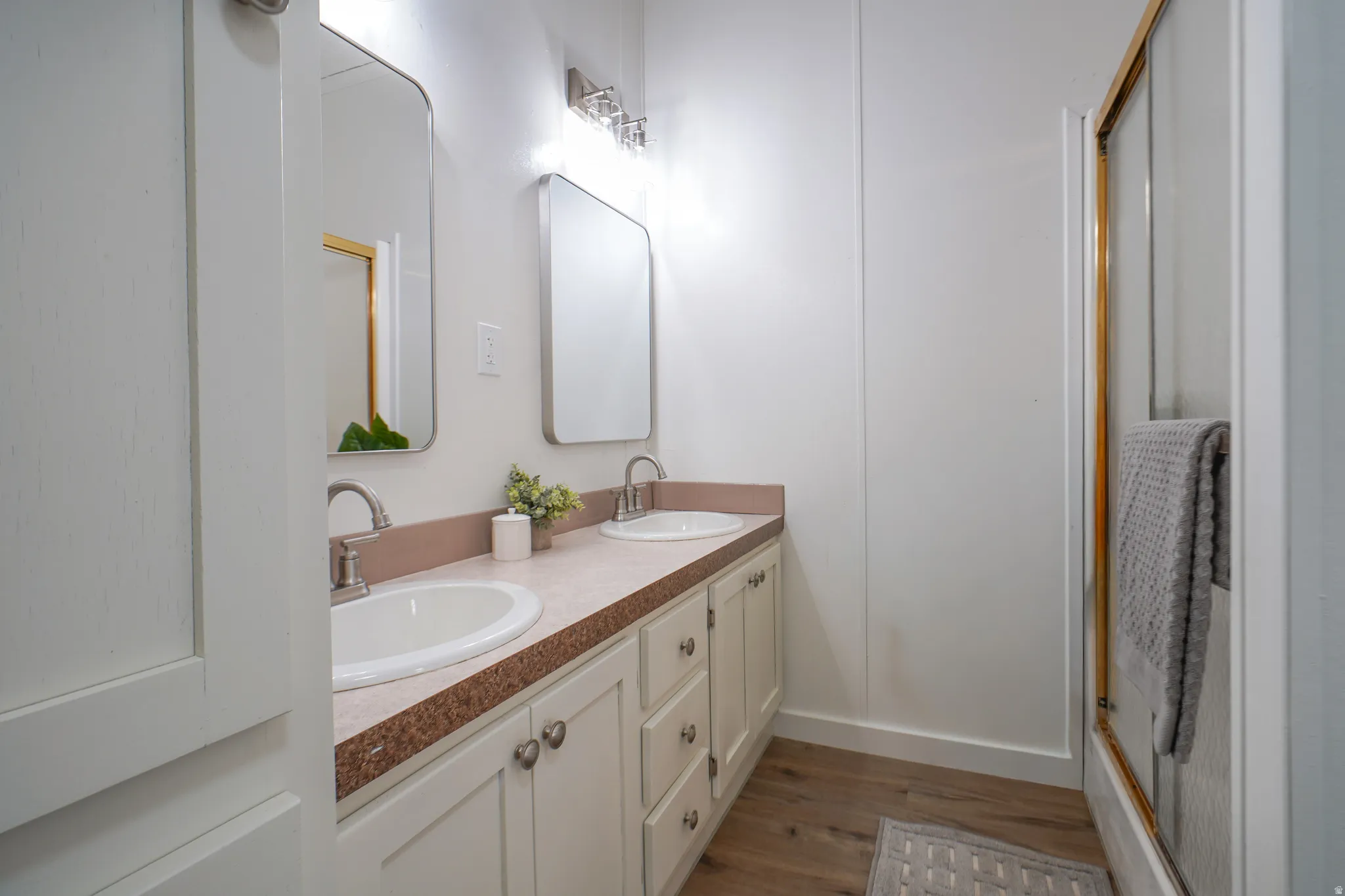 Dual vanity with undermount sinks, wood-finish flooring, and a shower enclosure