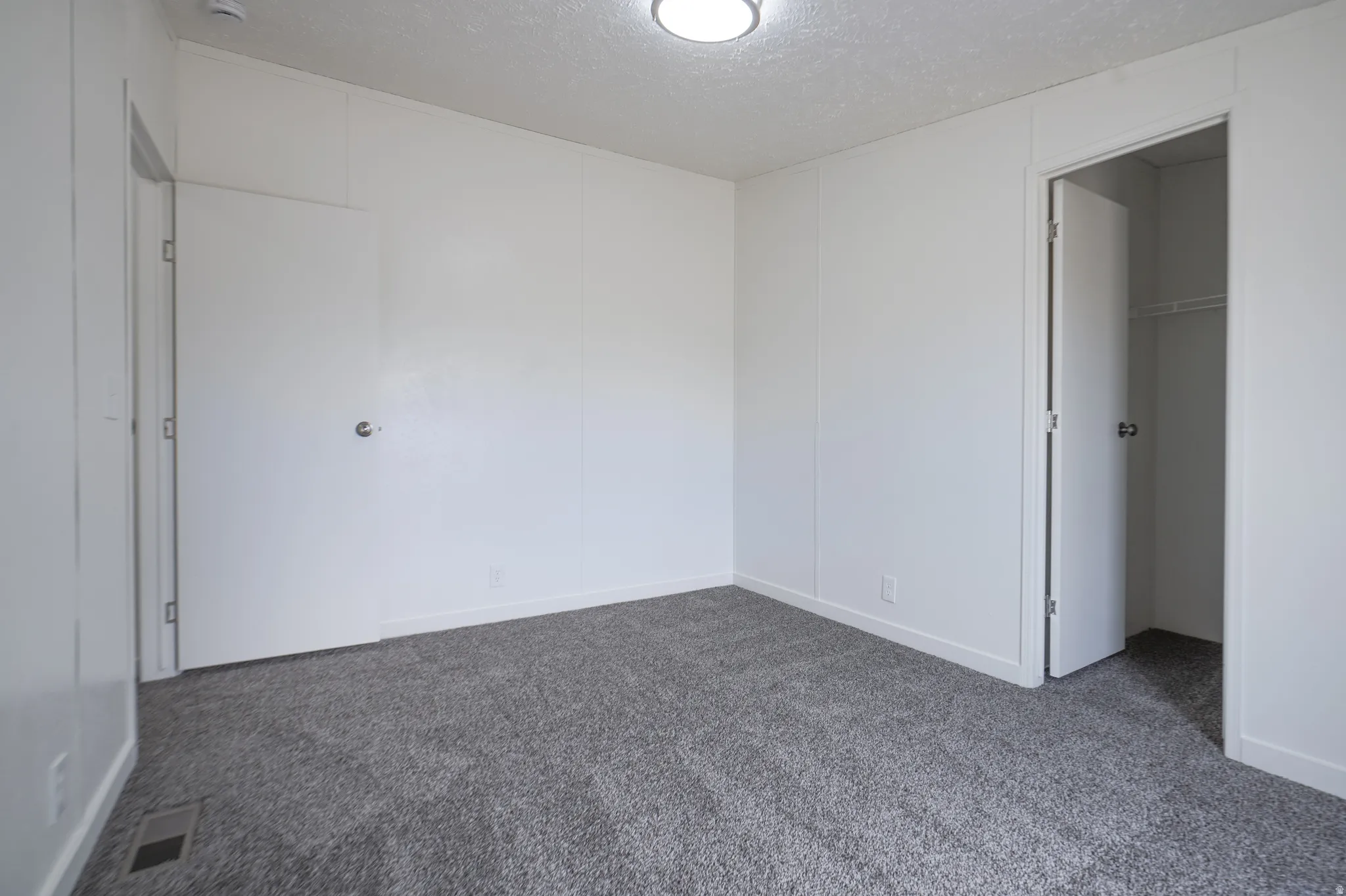 Light-colored walls, gray carpet, flush-mount ceiling light, and built-in closet with wire shelving