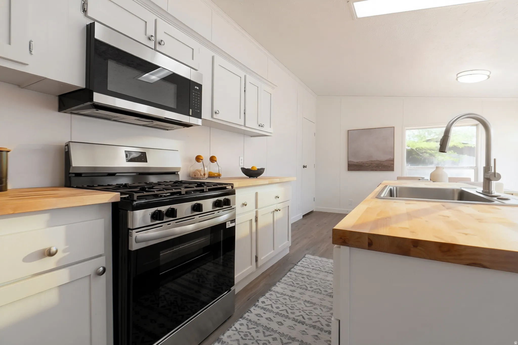 Stainless steel appliances, wood-finish countertops, white cabinetry, and an undermount sink with a gooseneck faucet