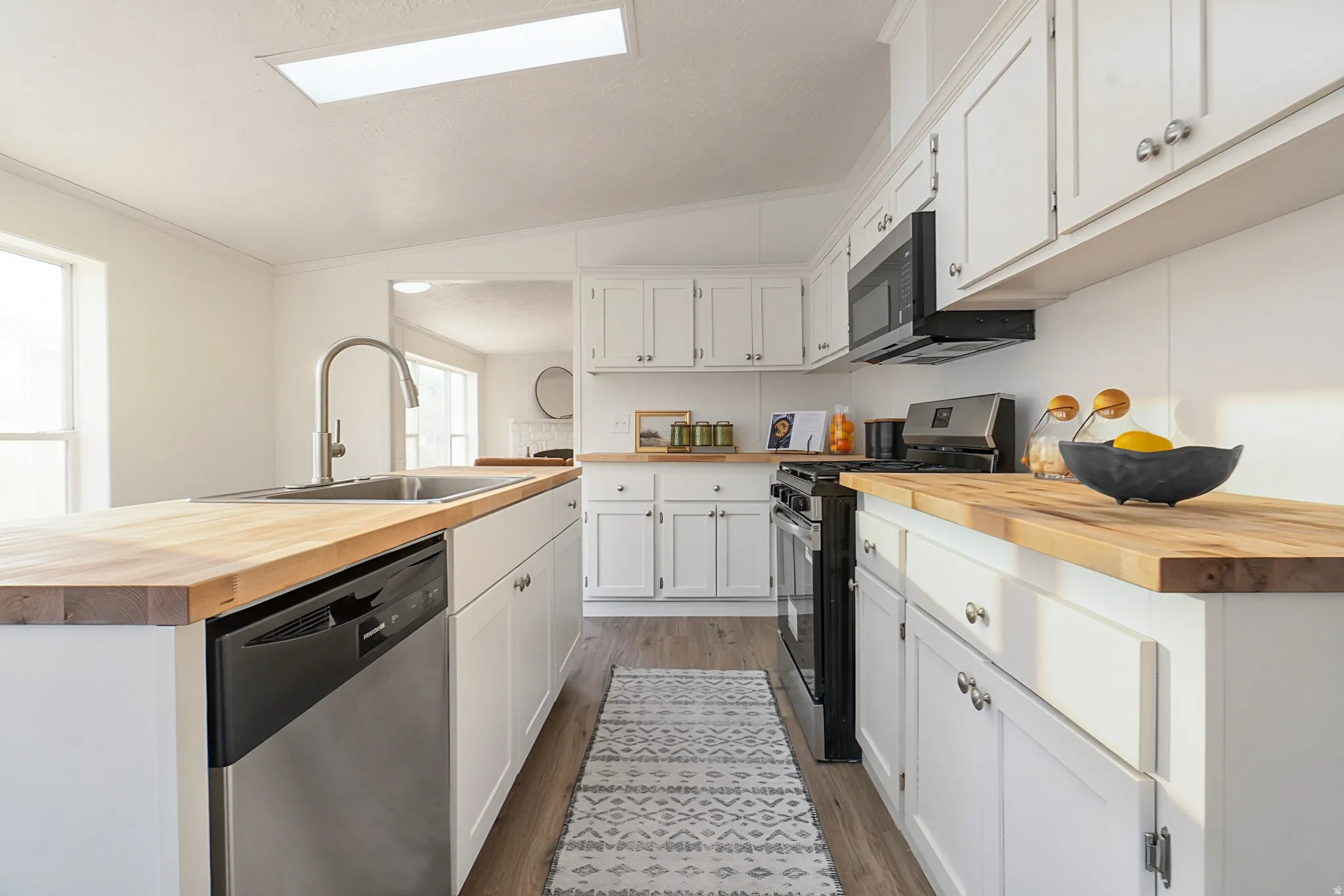 Galley kitchen featuring white cabinetry with brushed nickel hardware, wood-finish countertops, stainless steel appliances including a dishwasher and built-in oven, an arched gooseneck faucet, and recessed ceiling lighting throughout