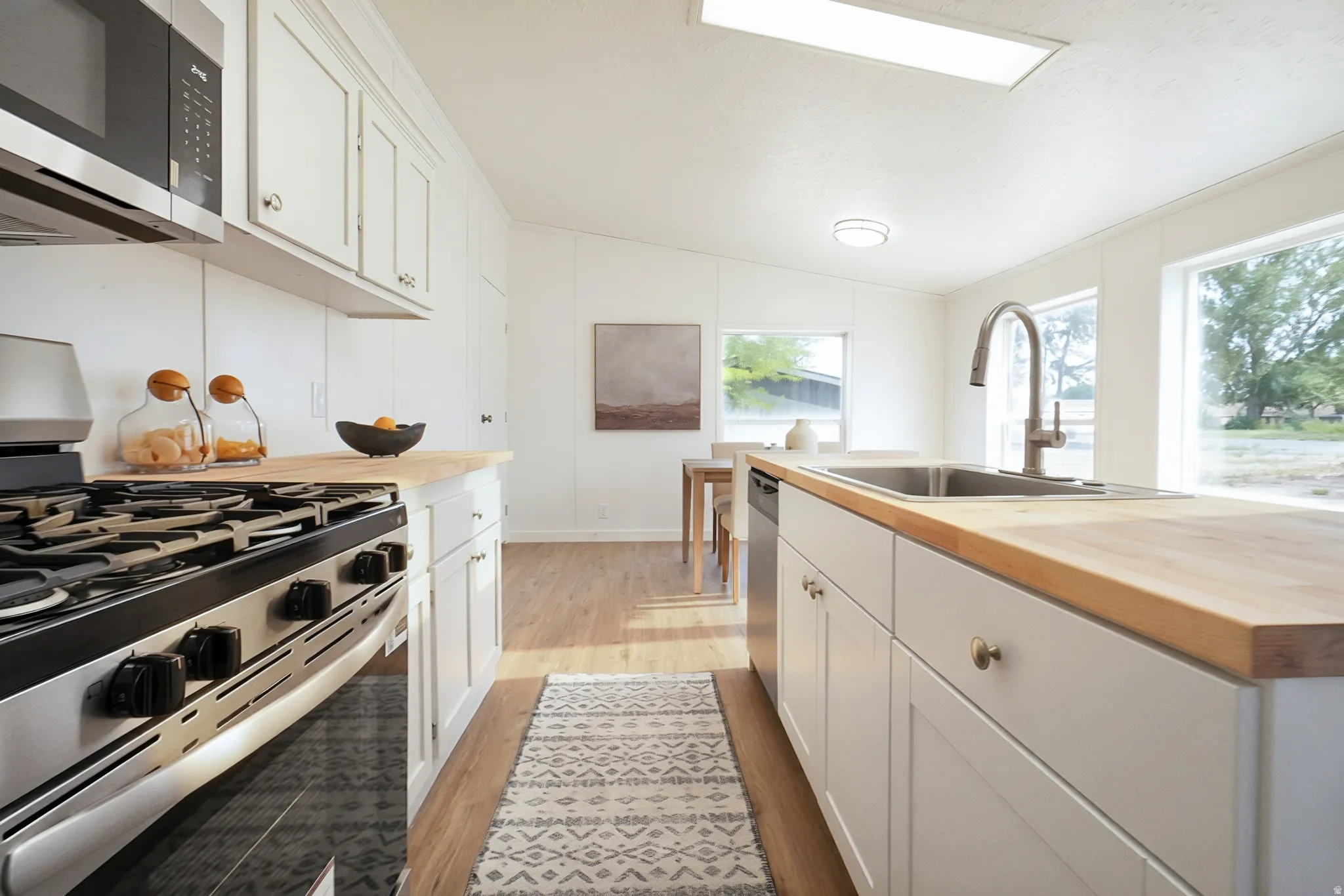 Bright kitchen featuring white cabinetry, wood-finish countertops, stainless steel appliances, and wood-finish flooring
