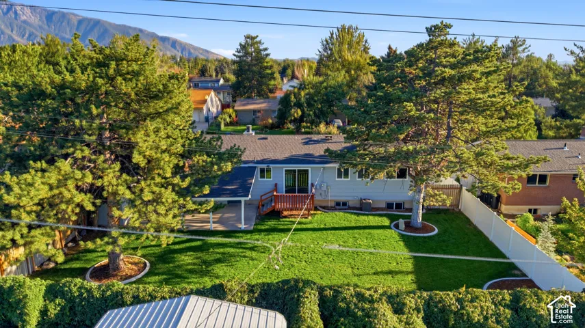 Expansive backyard featuring a large green lawn, mature trees, a wood deck, a covered patio, and mountain scenery