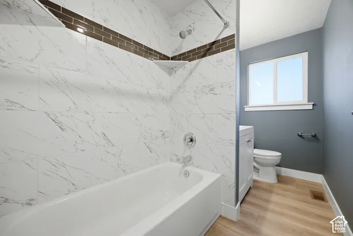 Bathtub with white and gray veined tile surround, subway tile accent band, and chrome fixtures