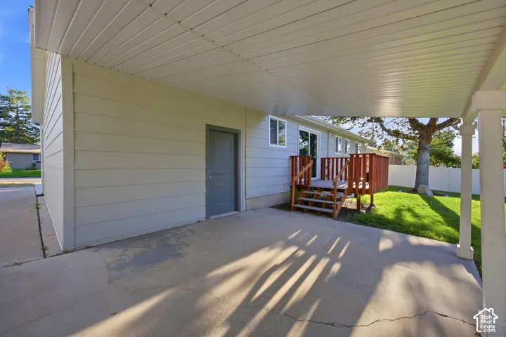 Covered concrete patio with white support columns, leading to a wooden deck with steps and railings