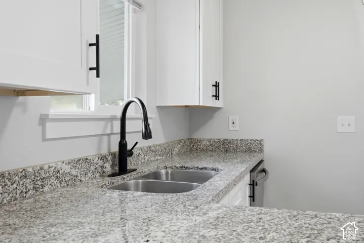 Granite countertops, dual basin stainless steel sink, matte black gooseneck faucet, white cabinetry, and a window