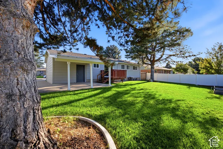 Expansive backyard featuring a lush lawn, mature trees, a covered patio, and privacy fencing