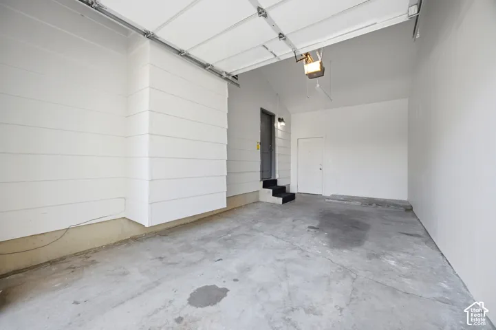 Concrete flooring with two entry doors, an automatic garage door opener, and a wall-mounted light fixture
