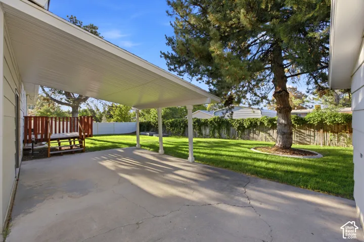 Expansive backyard featuring a covered patio, concrete surface, and a wooden deck