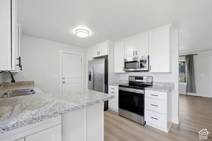 Modern kitchen featuring white cabinetry, stainless steel appliances including a built-in microwave and electric range, light-speckled quartz countertops, and warm wood-finish flooring throughout the open layout