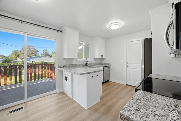 Kitchen featuring wood-finish flooring, white cabinetry, speckled countertops, stainless steel appliances, and a sliding glass door leading to a deck