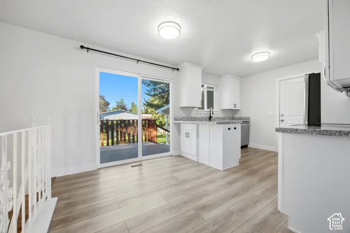 Kitchen featuring white cabinetry, light wood-finish flooring, granite-style countertops, stainless steel appliances, and a sliding glass door to a deck