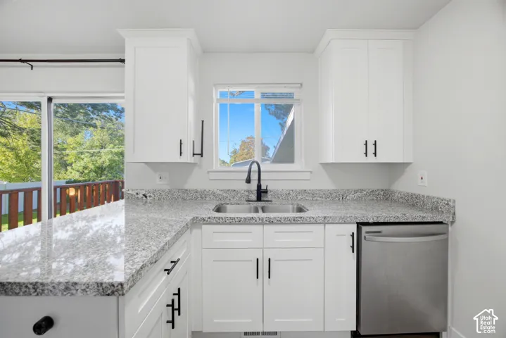 White shaker-style cabinetry with matte black hardware, dual basin stainless steel sink with a matte black faucet, integrated stainless steel dishwasher, and light-toned stone finish countertops