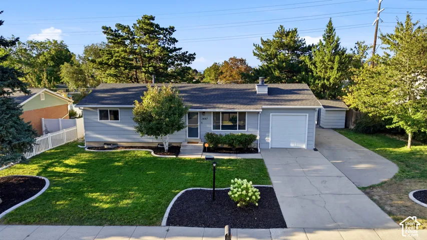 Light blue exterior with white trim, attached garage, concrete driveway, and mature landscaping