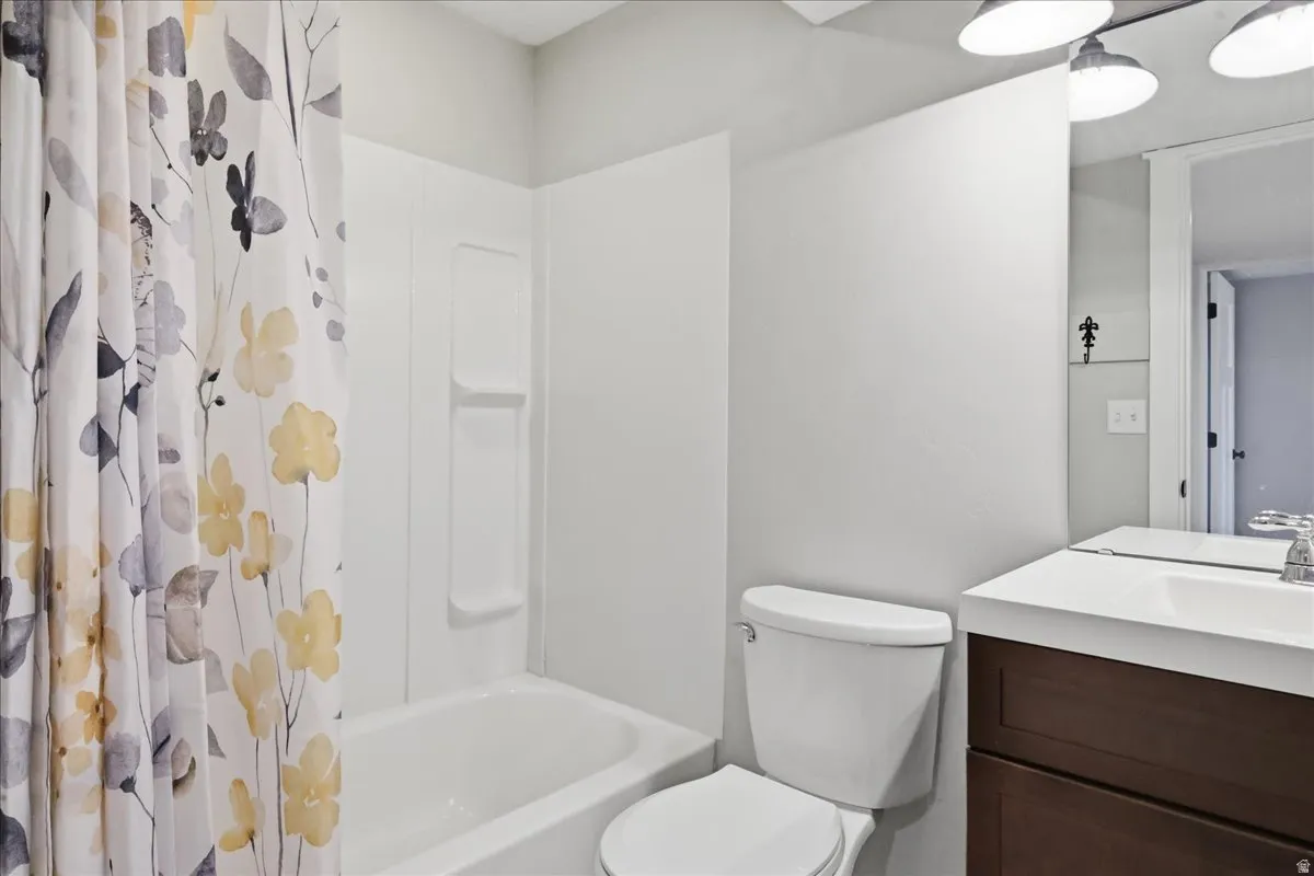 Built-in bathtub with a white surround and integrated shelving, white toilet, brown wood-finish vanity with a white countertop and integrated sink, and an overhead vanity light fixture