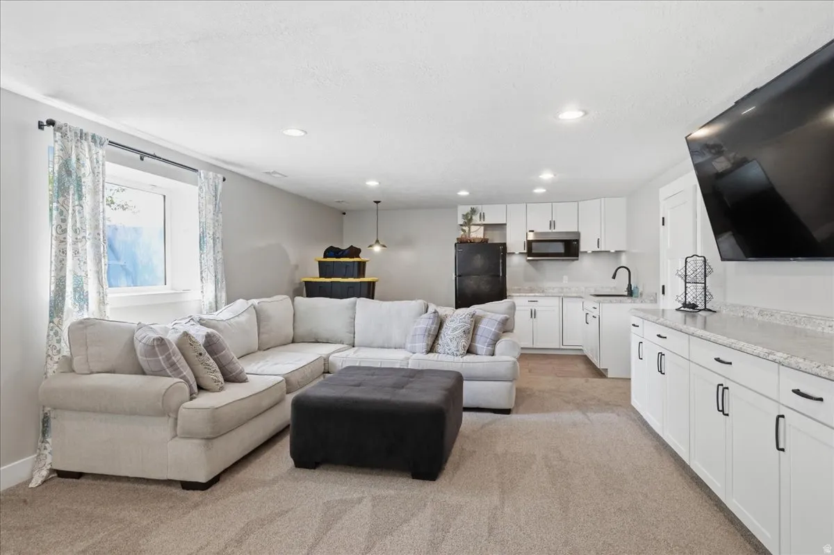 Finished space featuring carpet flooring, recessed lighting, a built-in wet bar with white cabinetry and light-toned countertops, and a kitchen area with white cabinetry, a black sink, and black appliances
