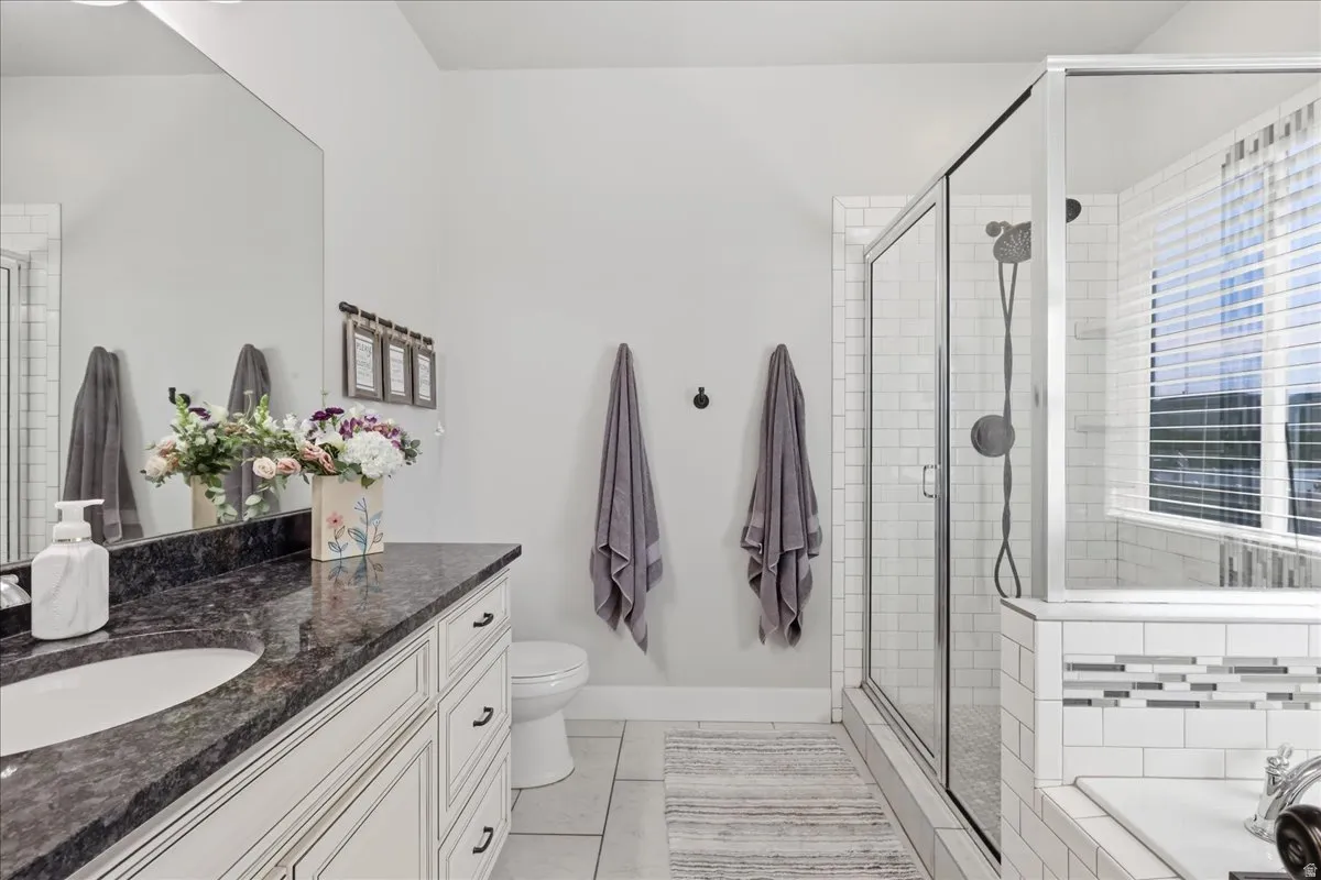 Spacious primary bathroom featuring a dark speckled countertop vanity with an integrated sink, a glass-enclosed shower with subway tile, and a built-in bathtub with decorative accent tiling