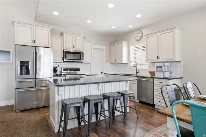Kitchen featuring white shaker cabinetry, stainless steel appliances, dark countertops, a subway tile backsplash, and dark wood-finish flooring