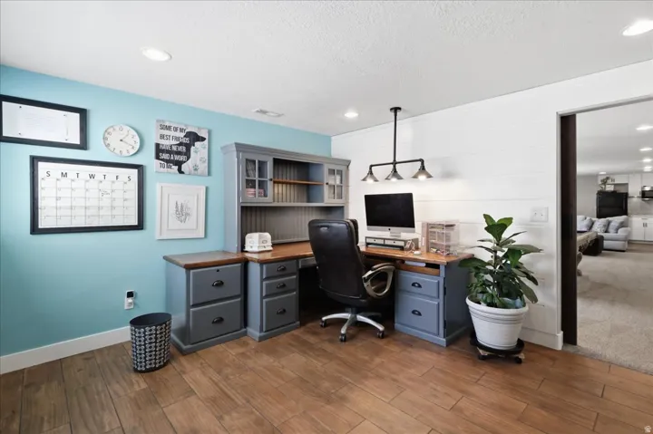 Wood-finish flooring, recessed lighting, and a built-in desk with overhead shelving