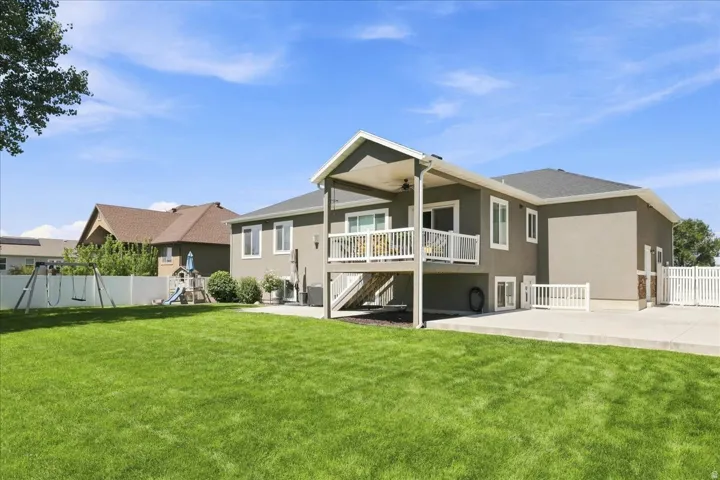 Expansive green lawn with a two-story stucco exterior, covered patio, upper-level deck with white railing, and a concrete patio space
