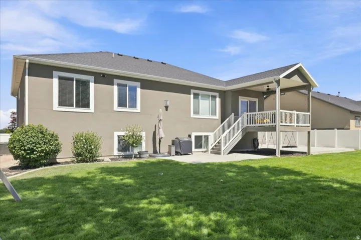 Expansive green lawn with a covered deck, white railing, and exterior staircase