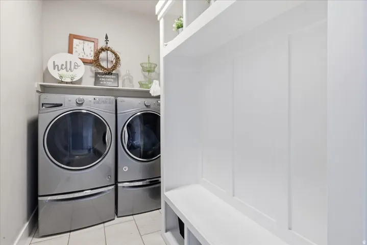 Built-in laundry appliances with a shelf, white tile flooring, and a built-in storage bench with paneling