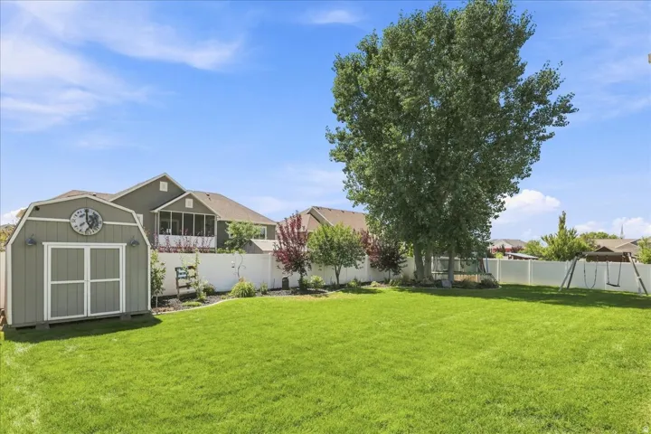 Expansive backyard featuring a manicured lawn, a detached storage shed, a white privacy fence, and mature trees