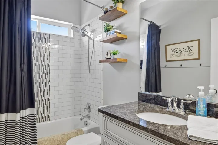White subway tile shower surround with a mosaic accent, a single vanity with a dark countertop, and a window above the shower