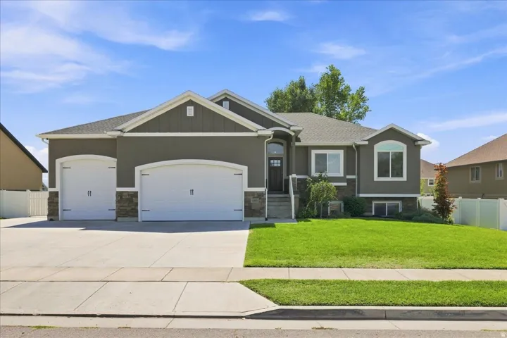 Stucco exterior featuring stone accents, a two-car garage with arched doors, a covered entry, and a front lawn