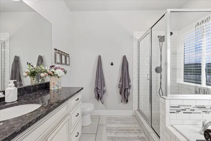 Spacious primary bathroom featuring a dark speckled countertop vanity with an integrated sink, a glass-enclosed shower with subway tile, and a built-in bathtub with decorative accent tiling