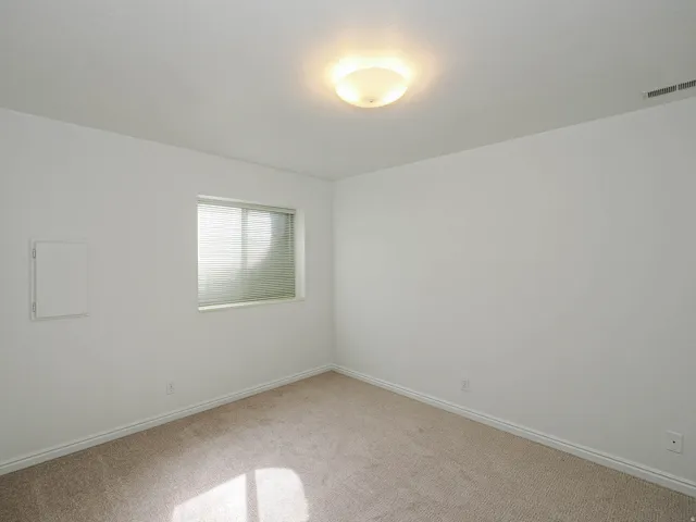 Bright, light-filled bedroom featuring neutral wall finishes, carpeted flooring, recessed ceiling lighting, and a large window with cellular shades providing natural illumination