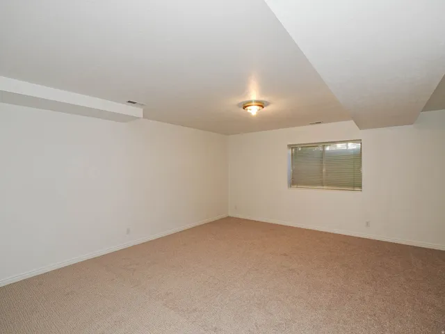 Spacious room featuring neutral carpet flooring and a single window with horizontal blinds