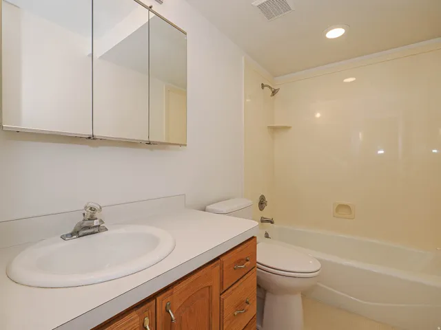 Bathroom featuring a vanity with a white countertop, wood-finish cabinetry, built-in medicine cabinet, and a shower/tub combination with an integrated soap dish