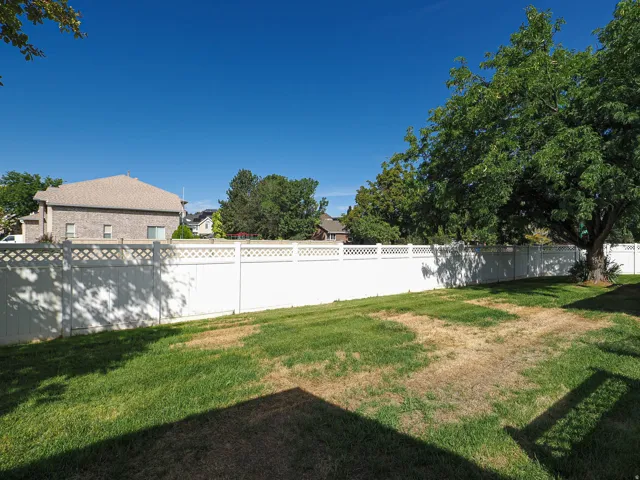 Expansive backyard with a full privacy fence featuring lattice accents and mature trees