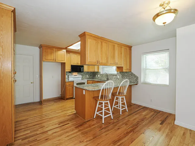 Kitchen featuring wood-finish flooring, wood cabinetry, granite countertops, and a built-in microwave
