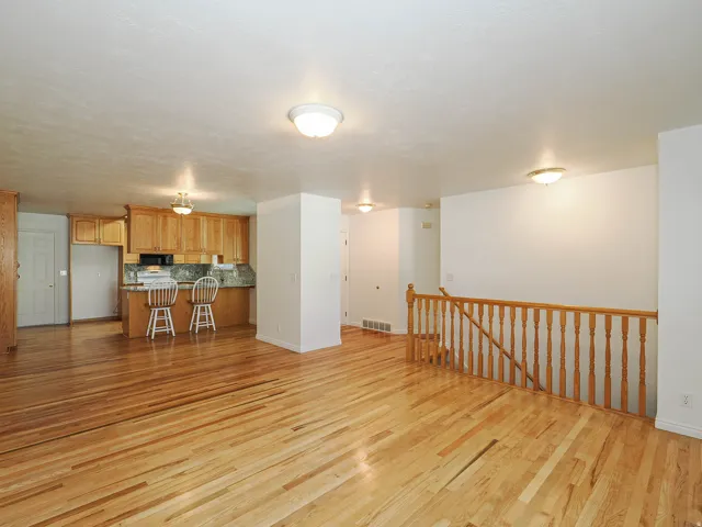 Hardwood flooring throughout, kitchen with wood cabinetry and stone-look countertops, built-in kitchen appliances, and a wood-spindle staircase