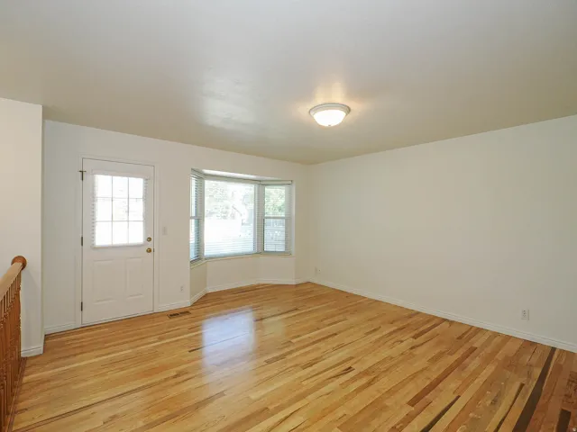 Light wood-finish flooring, white walls, bay window, white paneled door with glass inserts, and a flush-mount ceiling light