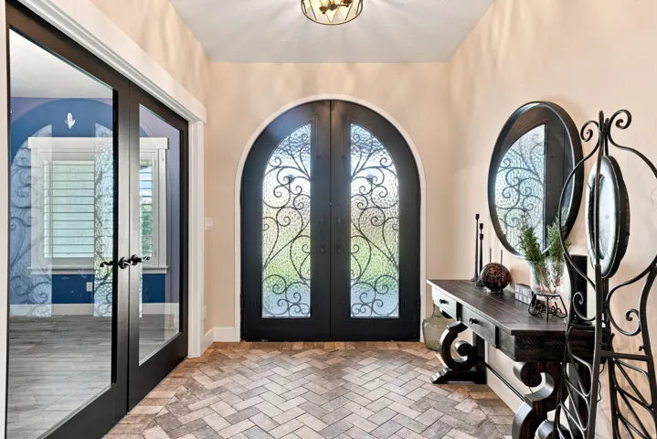 Arched entry doors with decorative ironwork, herringbone-patterned flooring, and dark-framed glass paneled doors