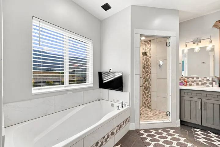 Freestanding soaking tub with tiled surround, walk-in shower with glass enclosure, single vanity with integrated sink, and hexagon tile accents
