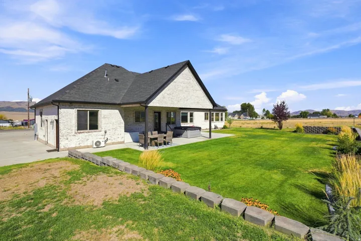 Spacious backyard with expansive green lawn, covered patio, and concrete paver retaining wall