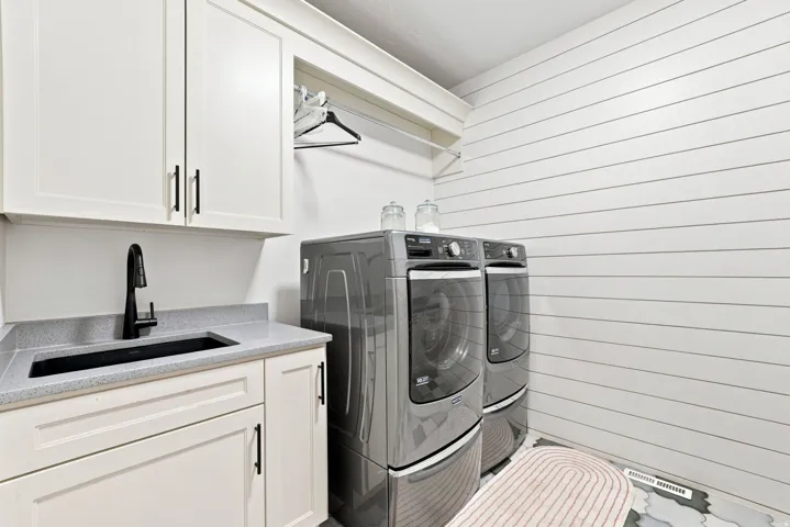 White shaker cabinetry, light-colored countertop, integrated sink with matte black faucet, and shiplap wall paneling