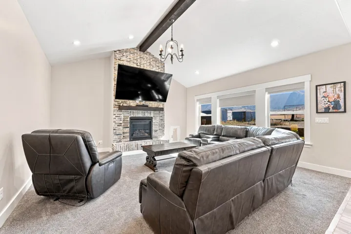 Vaulted ceiling with exposed beam, recessed lighting, stone-clad fireplace, and multiple windows