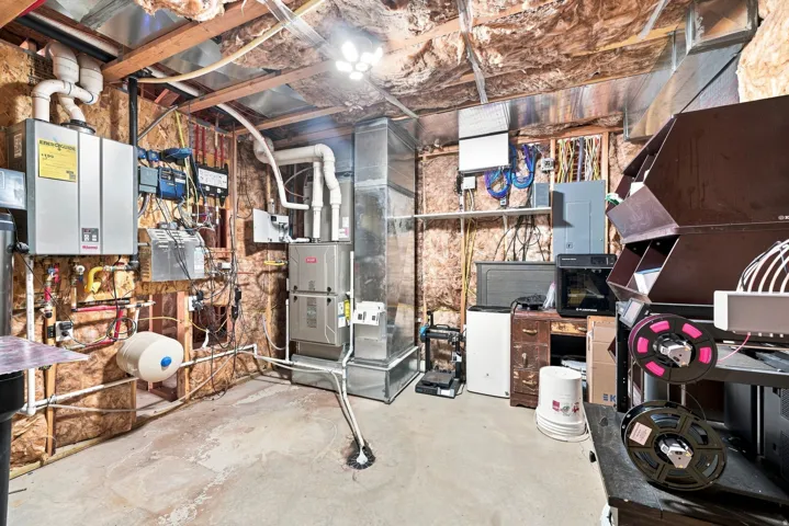 Exposed ceiling joists with insulation, utility room with HVAC unit, tankless water heater, and various electrical conduits