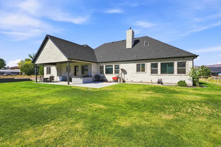 Expansive rear lawn with a covered patio, exposed aggregate patio, white brick exterior, and a dark shingle roof