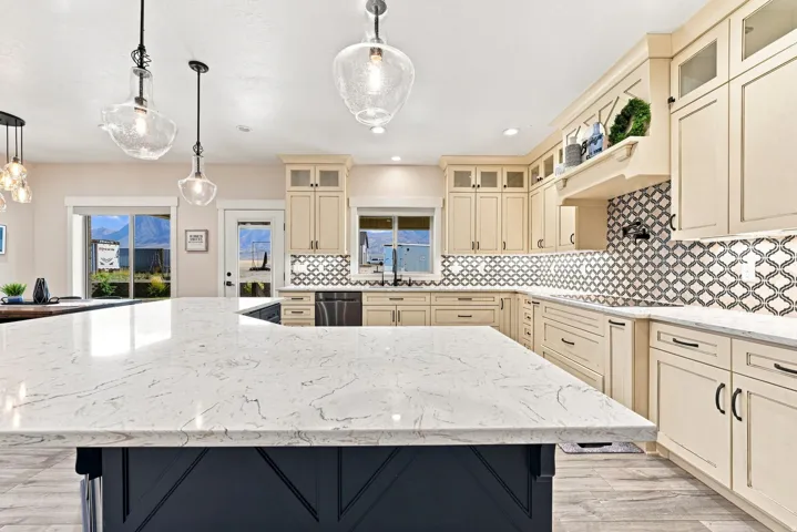 Spacious kitchen featuring a large central island with a light-toned countertop, extensive cabinetry, patterned tile backsplash, and stainless steel appliances