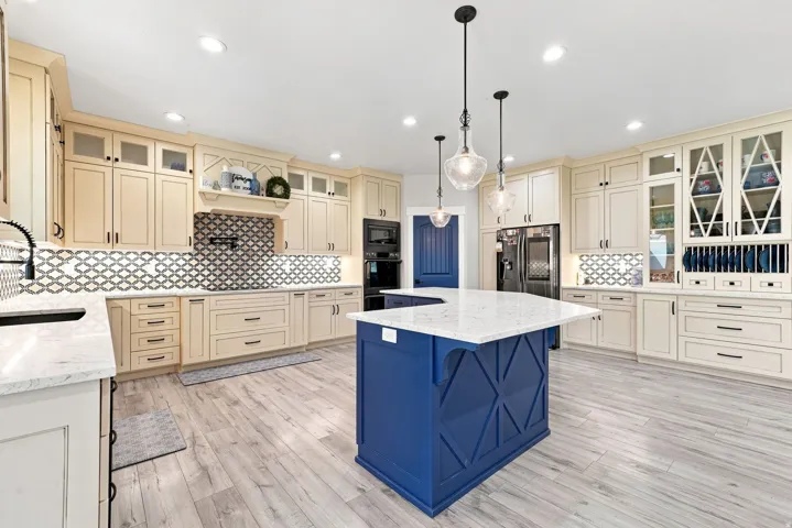 Spacious kitchen featuring an expansive center island with a stone countertop, light wood-finish flooring, and recessed ceiling lighting