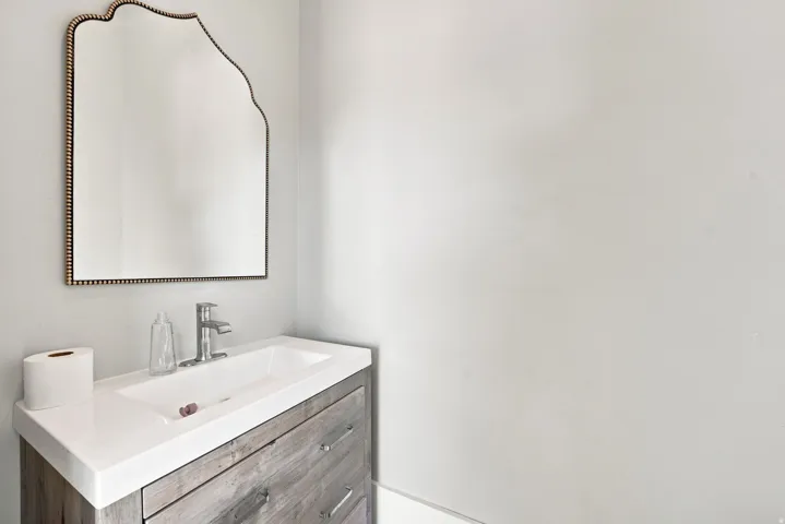 White rectangular undermount sink with a single-handle chrome faucet, set into a light wood-finish vanity with drawer pulls, topped by a light-colored countertop
